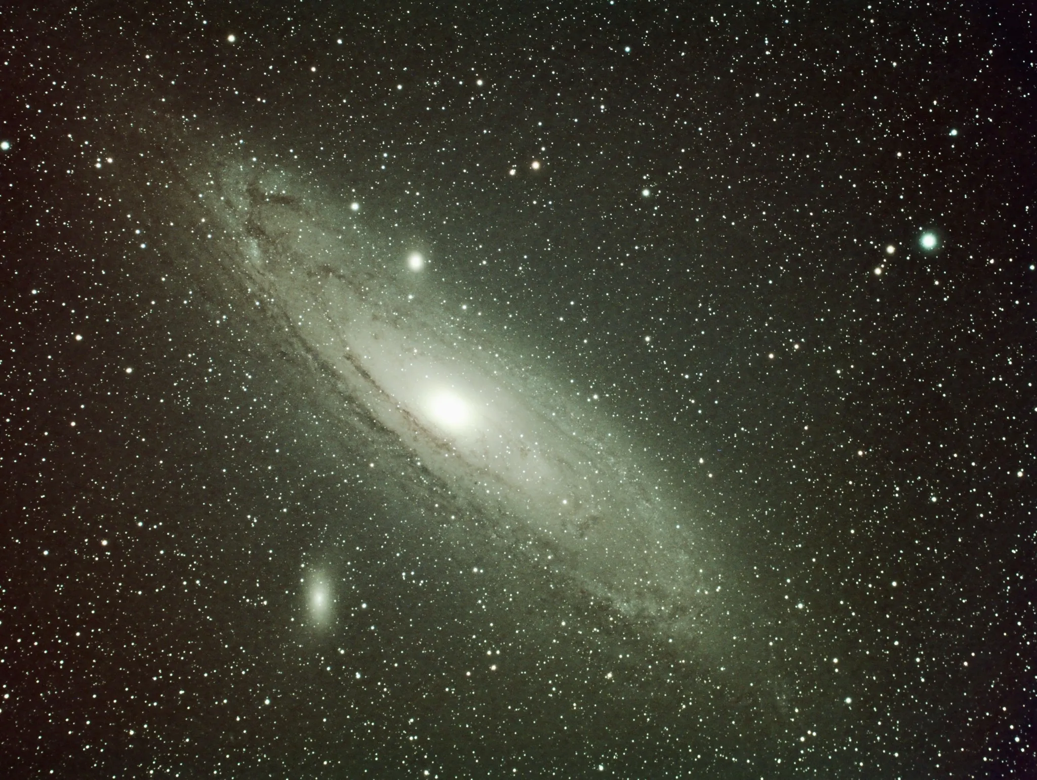 The Andromeda Galaxy, a bright tilted spiral with dust lanes crossing its disc, surrounded by dense foreground stars.